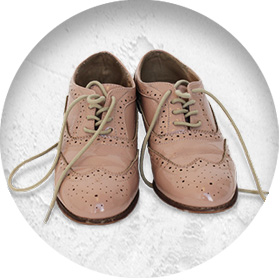 A photo of a pair of pinkish patent leather brogues, with punched hole patterns and beige laces.