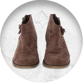 A photo of a pair of light brown suede chelsea boots with small tassles on the side