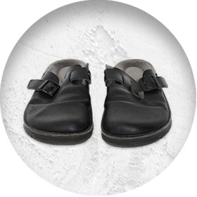 A photo of a pair of black leather backless slip-on shoes with a buckle detailing
