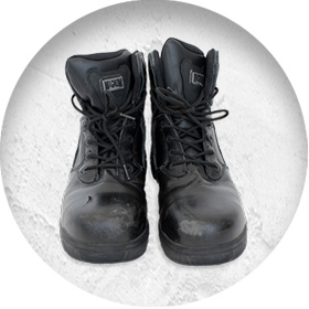 A photo of a pair of well-worn black workboots, with scuffs on the toes